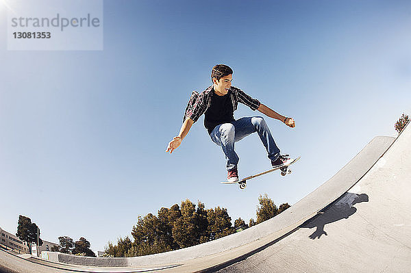Niedrigwinkelansicht eines Mannes  der im Skateboard-Park vor klarem blauen Himmel einen Stunt macht