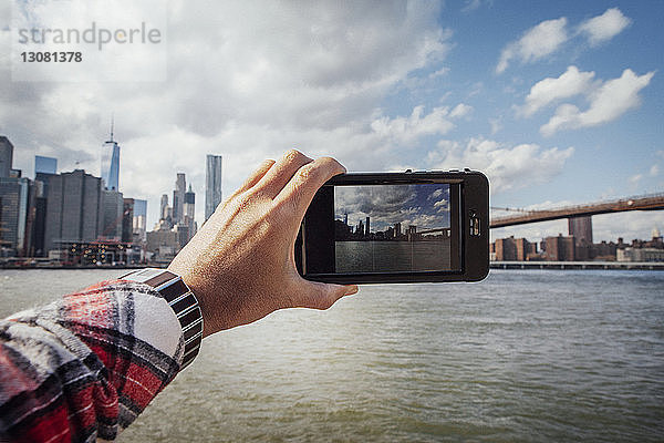 Ausgeschnittene Hand eines Mannes  der die Skyline und die Brooklyn Bridge fotografiert