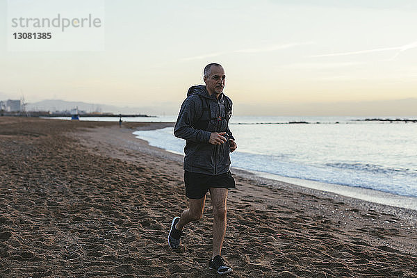 Mann joggt bei Sonnenuntergang am Strand gegen den Himmel