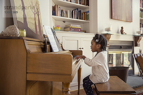 Seitenansicht eines klavierspielenden Mädchens im Wohnzimmer