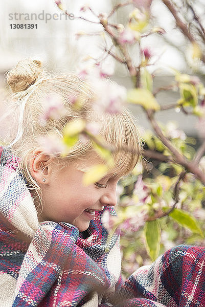 Nahaufnahme eines lächelnden  in eine Decke gehüllten Mädchens  das bei Pflanzen im Hof sitzt