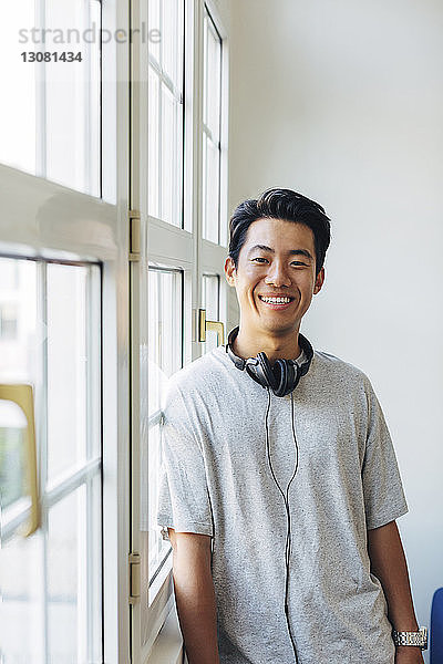 Porträt eines glücklichen Geschäftsmannes mit Kopfhörern am Fenster im Büro