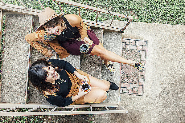 Draufsicht auf fröhliche Freundinnen  die auf Stufen sitzend Kaffee trinken