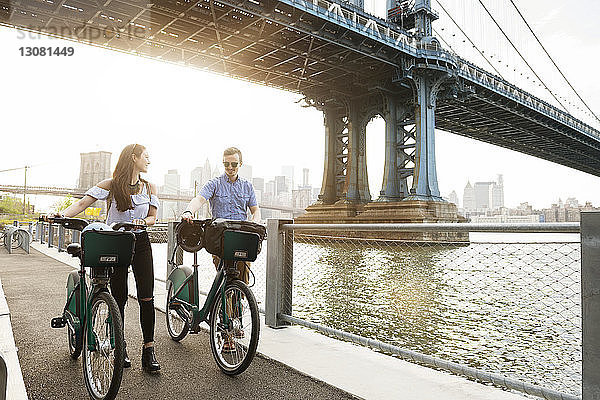 Paar zu Fuß mit Fahrrädern auf der Promenade am East River gegen die Manhattan-Brücke