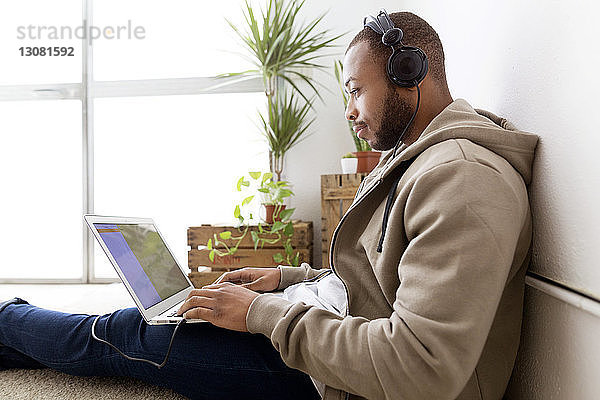 Seitenansicht eines kreativen Geschäftsmannes  der Musik hört  während er seinen Laptop im Büro benutzt