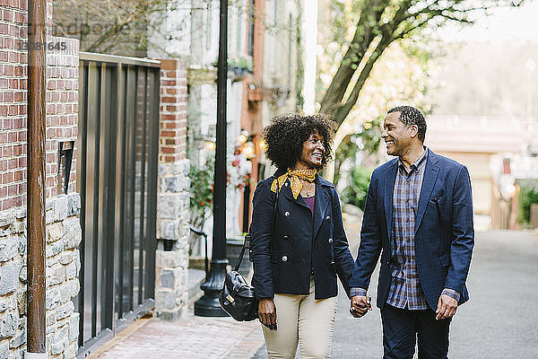 Glückliches Paar  das sich beim Gehen auf der Straße an den Händen hält und einander anschaut