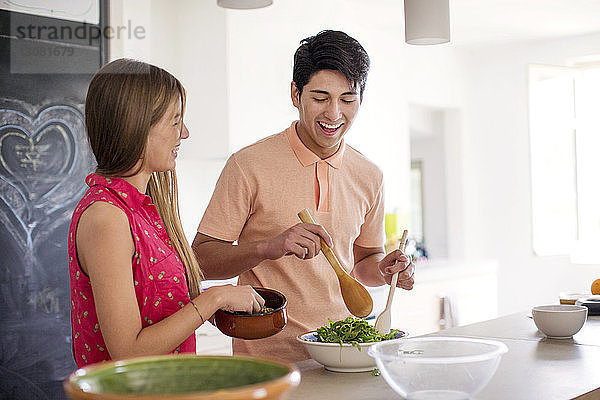 Glückliches Paar bereitet zu Hause in der Küche Salat zu