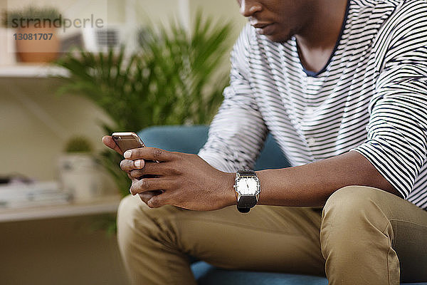 Mittelsektion eines Mannes  der ein Smartphone benutzt  während er zu Hause auf dem Sofa sitzt