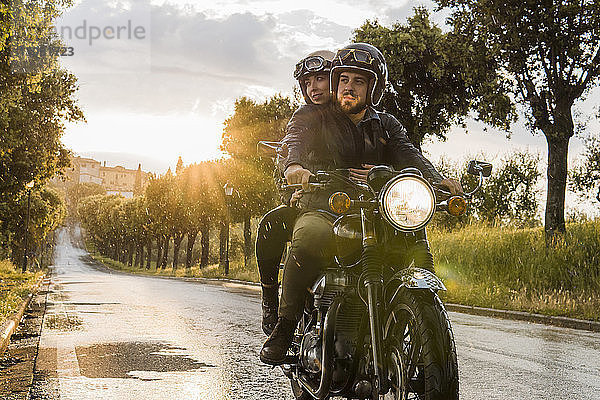 Paar  das bei Sonnenuntergang auf dem Motorrad sitzend gegen den Himmel schaut