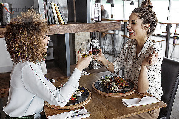 Fröhliche Geschäftsfrauen stoßen am Tisch im Restaurant auf Weingläser an