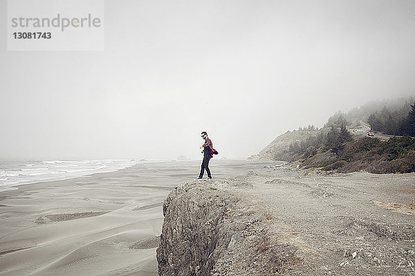 Seitenansicht eines Mannes  der bei nebligem Wetter auf einer Klippe am Strand steht