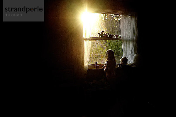 Geschwister schauen durch das Fenster  während sie zu Hause in der Dunkelkammer stehen