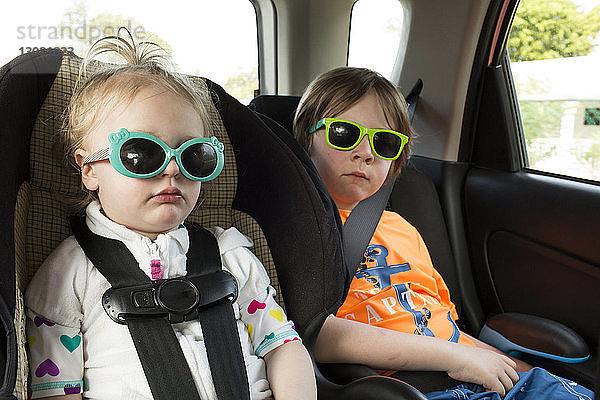 Geschwister mit Sonnenbrille im Auto unterwegs