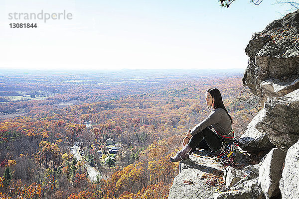 Seitenansicht einer Frau  die auf einem Felsen gegen den Himmel sitzt