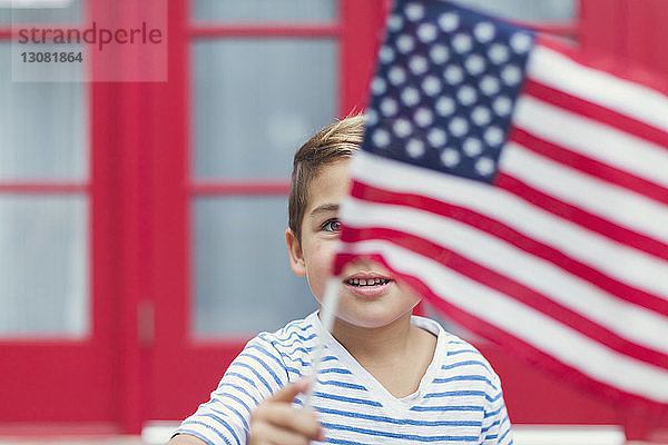 Nahaufnahme eines Jungen  der die amerikanische Flagge schwenkt  während er gegen das Haus steht