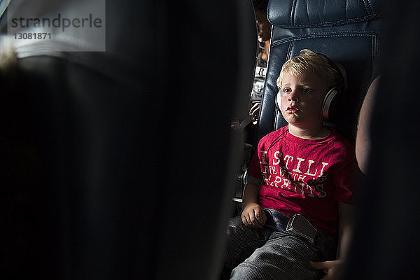 Junge schaut weg  während er im Flugzeug Musik hört