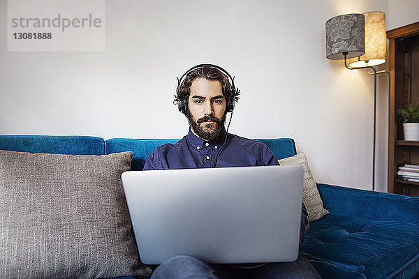 Geschäftsmann trägt Kopfhörer mit Laptop auf dem Sofa im Büro