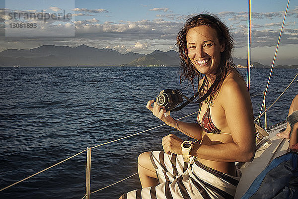 Porträt einer glücklichen Frau mit Kamera  die in einem Boot auf See reist