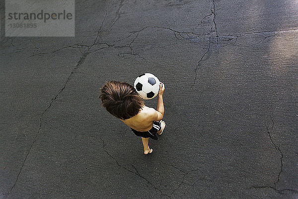 Draufsicht eines Jungen  der beim Gehen auf der Straße einen Fußball hält
