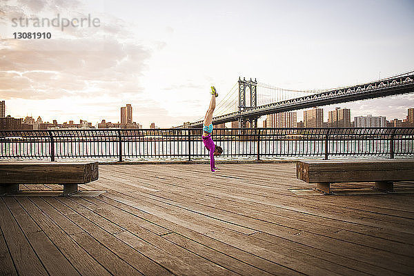 Frau macht Handstand bei Promenade gegen Manhattan-Brücke