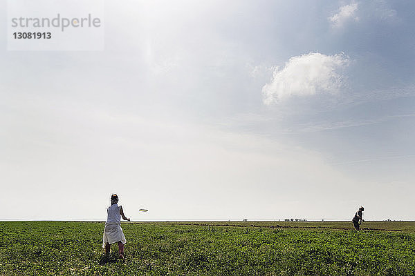 Paar spielt mit fliegender Scheibe auf Grasfeld gegen den Himmel