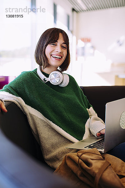 Porträt einer lächelnden Frau  die einen Laptop-Computer benutzt  während sie auf dem Sofa in der Bibliothek sitzt