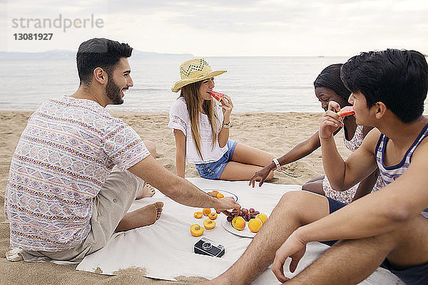 Glückliche Freunde essen Früchte  während sie am Strand sitzen