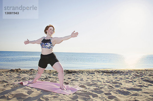 Frau in voller Länge am Strand bei klarem Himmel Yoga praktizierend