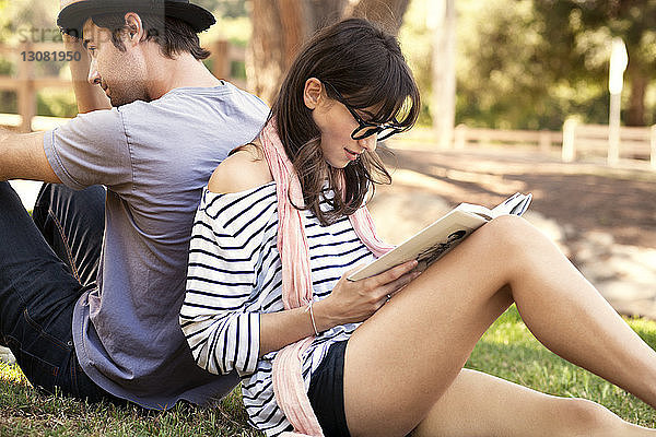Frau liest Buch  während sie mit Mann im Park sitzt
