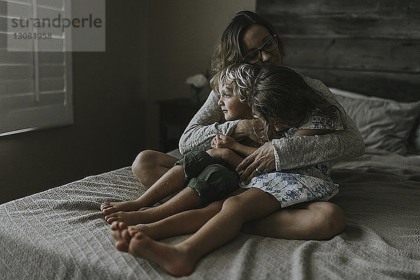 Frau umarmt Kinder  während sie auf dem Bett sitzt