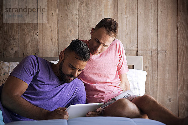 Homosexuelles Paar benutzt einen Tablet-Computer  während es auf dem Bett im Resort liegt