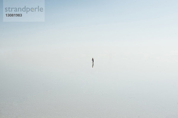 Hochwinkelaufnahme einer Frau  die bei nebligem Wetter im See gegen den Himmel steht