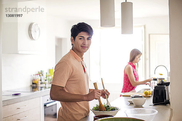 Porträt eines Salat zubereitenden Mannes mit im Hintergrund stehender Frau in der Küche