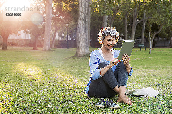 Lächelnde Frau benutzt digitales Tablett  während sie auf einem Grasfeld sitzt