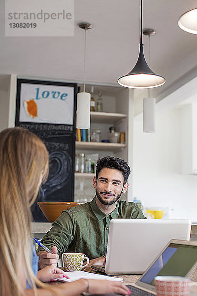 Lächelnder Mann schaut Frau an  während er zu Hause einen Laptop benutzt