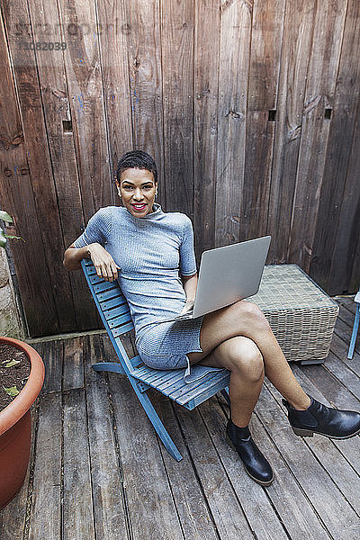 Porträt einer lächelnden Geschäftsfrau mit Laptop auf einem Stuhl sitzend