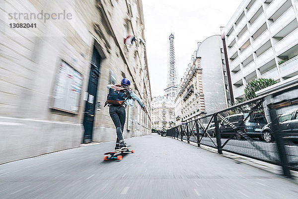 Rückansicht in voller Länge der Skateboard fahrenden Frau auf dem Fußweg vor dem Eiffelturm