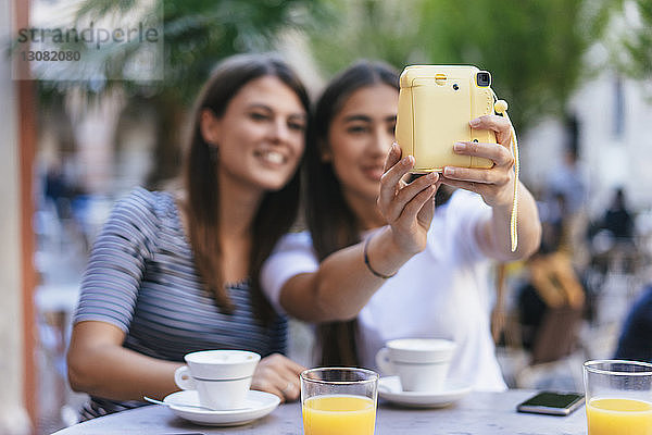 Freundinnen  die sich mit einer Sofortbildkamera selbst fotografieren  während sie im Straßencafé sitzen