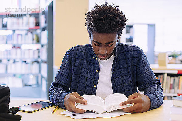 Mann liest Buch  während er in der Bibliothek am Tisch sitzt