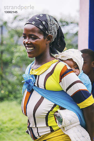 Fröhliche afrikanische Frau  die ein Mädchen in Stoff trägt