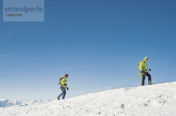 Seitenansicht von Wanderern  die auf einem schneebedeckten Berg bei strahlend blauem Himmel wandern