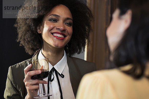 Lächelnde Frau unterhält sich mit einem Freund bei einem Glas Wein zu Hause