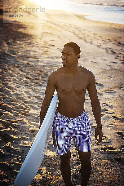 Mann mit Surfbrett schaut weg  während er am Strand auf Sand läuft