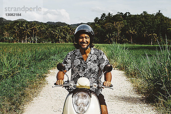 Porträt eines lächelnden Motorrad fahrenden Mannes auf unbefestigter Straße gegen den Himmel