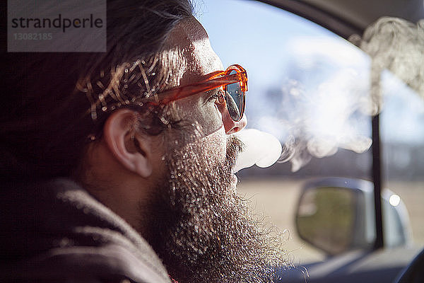 Seitenansicht eines männlichen Hipsters  der während des Urlaubs im Auto raucht