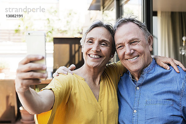 Fröhliches älteres Paar  das sich auf der Veranda per Smartphone selbstständig macht