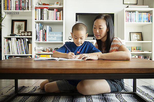 Frau unterstützt Sohn beim Lernen  während sie zu Hause auf dem Boden sitzt