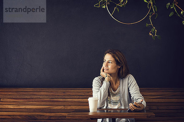 Nachdenkliche Frau schaut weg  während sie an einem Café-Tisch sitzt