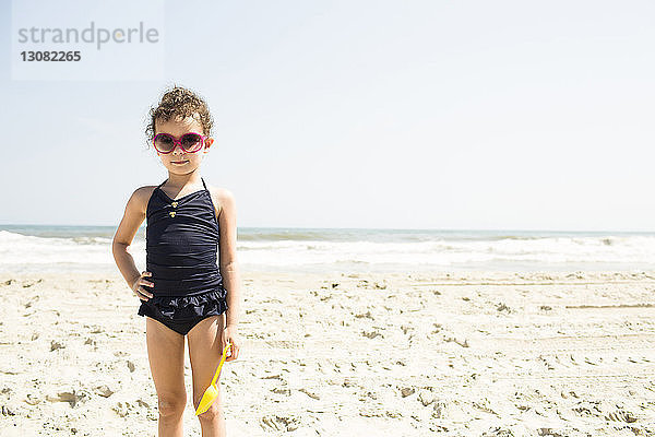 Porträt eines Mädchens in Badebekleidung mit Sonnenbrille  das bei Sonnenschein am Strand steht