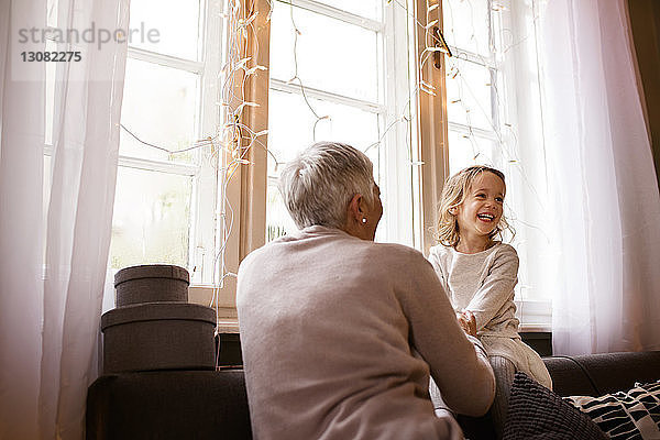 Glückliche Großmutter und Enkelin sitzen zu Hause auf dem Sofa